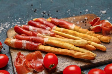 Lezzetli İtalyan Grissini ahşap tahtası ve arka planda pastırma.