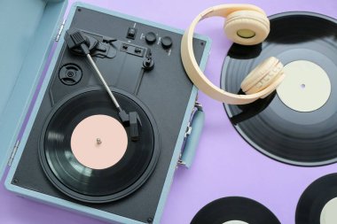 Eflatun arka planda vinil diskleri ve kulaklıkları olan kayıt çalar