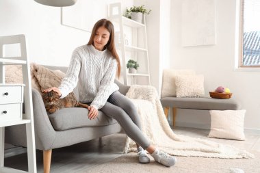 Evde çizgili İskoç kedisi olan genç bir kadın var.