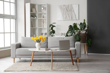 Modern dizüstü bilgisayarı ve kahve masasında vazosu olan şık bir oturma odası.