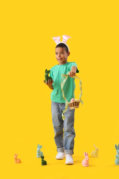 黄色の背景にイースターエッグとウサギのバスケットを持つ小さなアフリカ系アメリカ人の少年 — ストック写真
