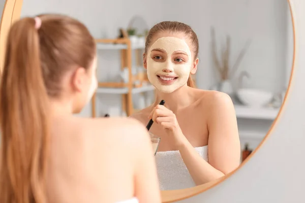 Jovem Mulher Aplicando Máscara Cúrcuma Com Escova Perto Espelho Casa — Fotografia de Stock