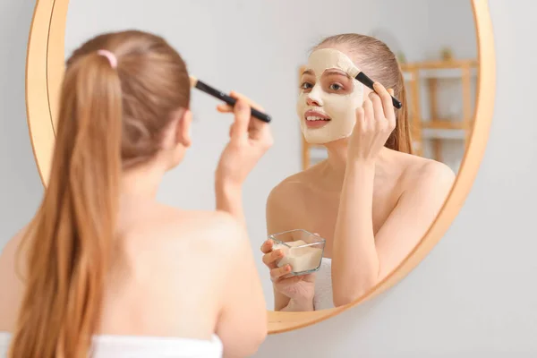 Jovem Mulher Aplicando Máscara Cúrcuma Com Escova Perto Espelho Casa — Fotografia de Stock