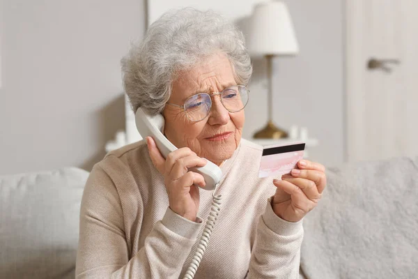 Senior woman with credit card talking by telephone at home, closeup