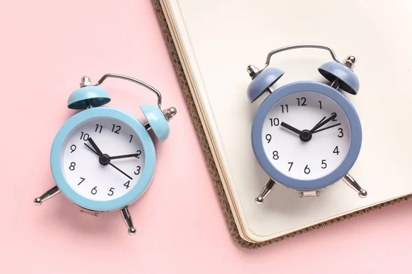 ピンクの背景の目覚まし時計とノートブック クローズアップ — ストック写真