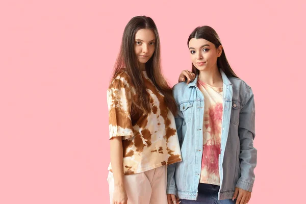 Stylish young women in tie-dye t-shirts on pink background