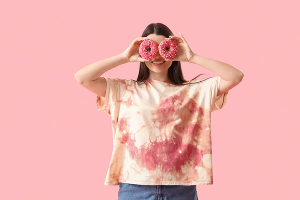 Funny young woman in tie-dye t-shirt and with donuts on pink background