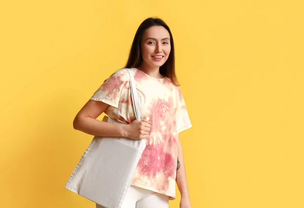 Stylish young woman in tie-dye t-shirt and with bag on yellow background