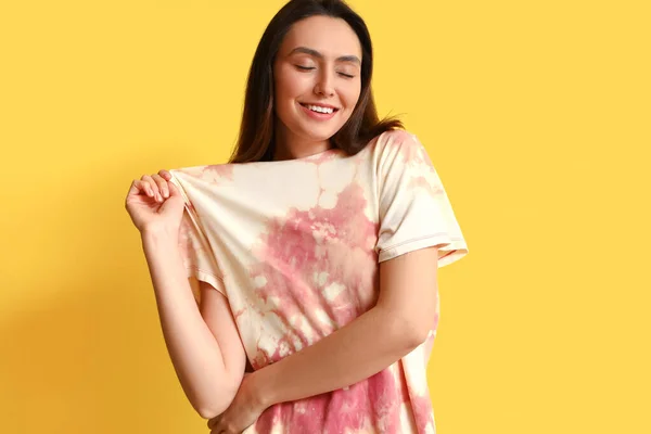 Stylish young woman in tie-dye t-shirt on yellow background