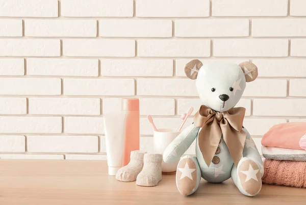 Leksaksbjörn Med Babykläder Och Tillbehör Bord Nära Vit Tegelvägg — Stockfoto