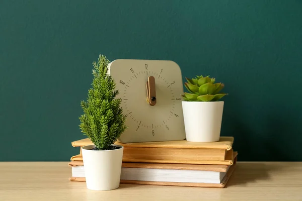 Artificial plants with clock and books on table near green wall