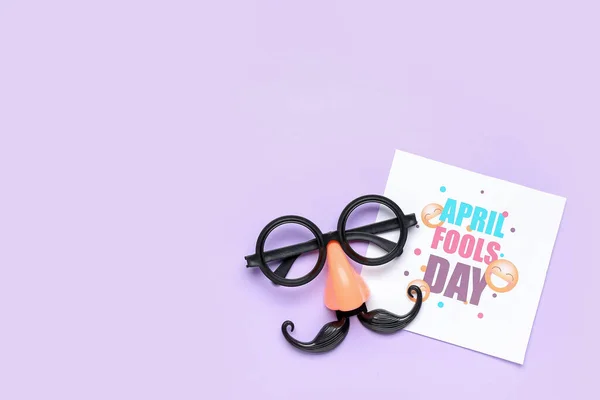 Card with text APRIL FOOLS DAY and funny disguise on lilac background