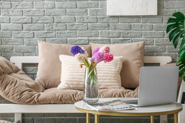Modern laptop, vase with hyacinth flowers and magazine on coffee table in living room