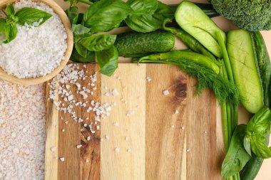 Tahta kesme tahtası, taze sebzeler, şifalı otlar ve bir kase deniz tuzu, yakın plan.