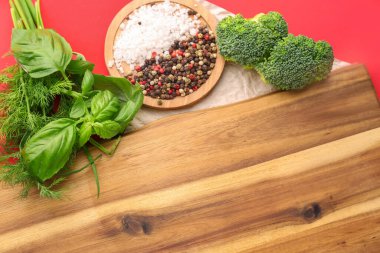 Kırmızı arka planda taze otlar, baharatlar ve brokoli bulunan ahşap tahta pano, yakın plan.