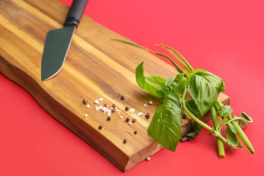 Ahşap tahta, otlar, baharatlar ve kırmızı arka planda bıçak, yakın plan.