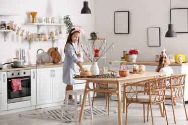 Küçük bir kız mutfakta paskalya yumurtalarıyla ağaç dalları süslüyor.