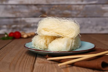 Çiğ pirinç şehriyeli tabak ve ahşap masada çubuklar.