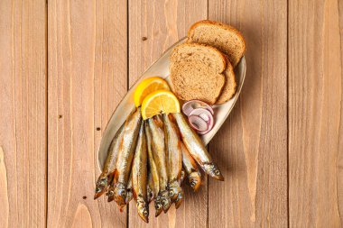 Lezzetli füme kapelinli tabak, ahşap zemin üzerinde limon ve ekmek dilimleri.