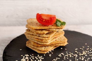 Tahta tahta üzerinde lezzetli krakerler, domates ve susam tohumları.