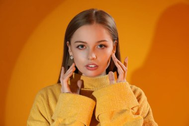 Fashionable young woman in knitted sweater on orange background