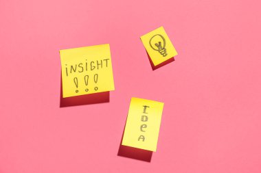 Sözcüklerle dolu yapışkan kağıtlar ve pembe arka planda çizilmiş ampul. İçgörü kavramı