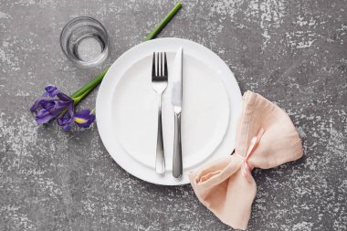 Temiz tabak, çatal bıçak takımı ve gri grunge masasında güzel bir orkide çiçeği.