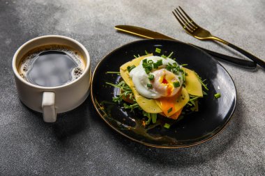 Lezzetli yumurtalı Benedict tabağı ve arka planda bir fincan kahve.