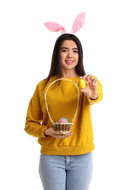 Beyaz arka planda Paskalya yumurtası sepeti olan tavşan kulaklı genç bir kadın.