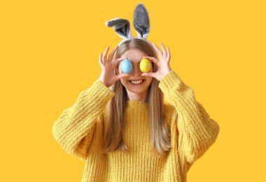 Sarı arka planda Paskalya yumurtaları olan tavşan kulaklı genç bir kadın.