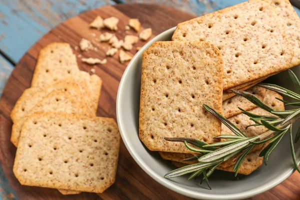 stock image Bowl with tasty crackers and rosemary on wooden board, closeup