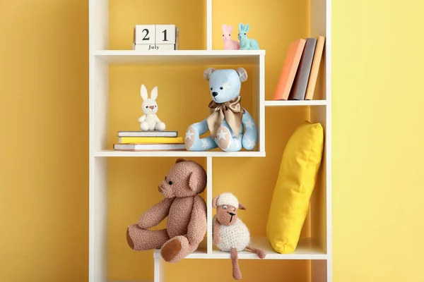 Bookshelf with baby toys near yellow wall