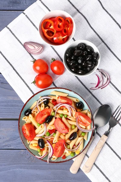 Bowl with tasty pasta salad and ingredients on blue wooden background