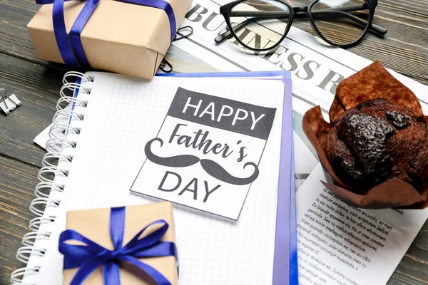 stock image Greeting card with text HAPPY FATHER'S DAY, notebook, newspaper, muffin and gifts on wooden table, closeup