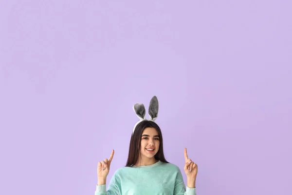 小兔子耳朵里的年轻女人指着紫丁香背景上的什么东西 复活节庆祝活动 — 图库照片