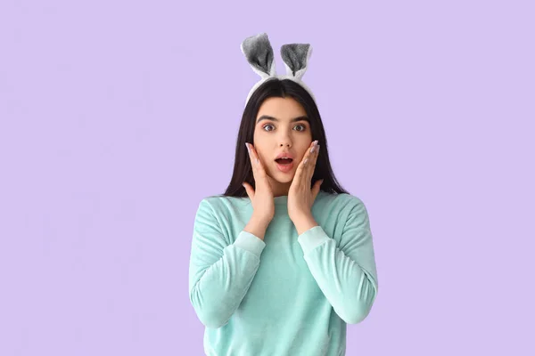 Surprised young woman in bunny ears on lilac background. Easter celebration