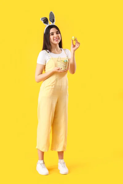 Mladá Žena Králičí Uši Košíkem Velikonočních Vajec Žlutém Pozadí — Stock fotografie