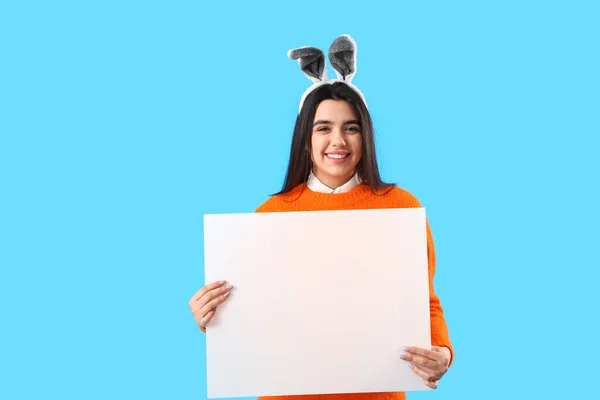 青い背景に空白の紙のシートを持つウサギの耳の若い女性 イースターのお祝い — ストック写真