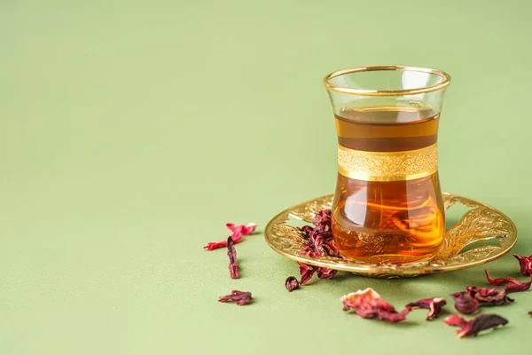Glass cup of Turkish tea with dry hibiscus leaves on color background