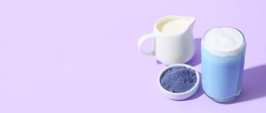 Bir bardak mavi kibrit çayı, sütlü sürahi ve eflatun arkaplanda bir kase toz ve metin için yer var.