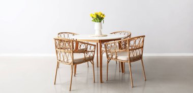 Yemek masasında sarı laleler ve aydınlık odada hasır sandalyeler olan vazo.