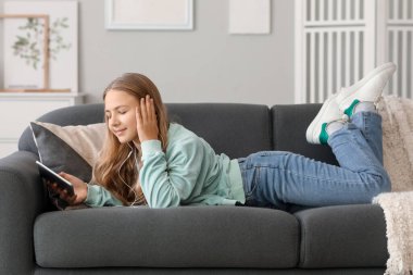 Little girl in earphones using tablet computer on sofa at home