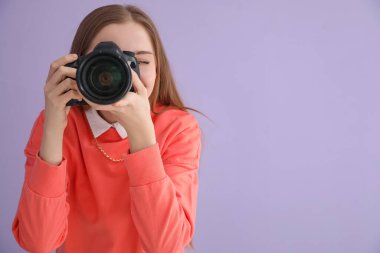 Eflatun arka planda profesyonel kamerası olan genç bayan fotoğrafçı.