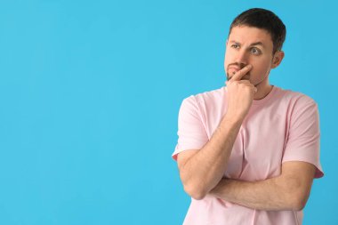 Mavi arka planda tişörtlü düşünceli genç adam.