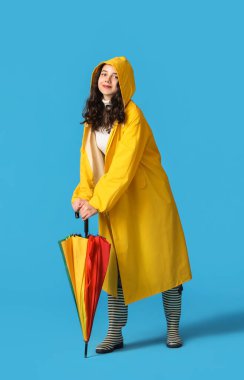 Teenage girl in raincoat with umbrella on blue background
