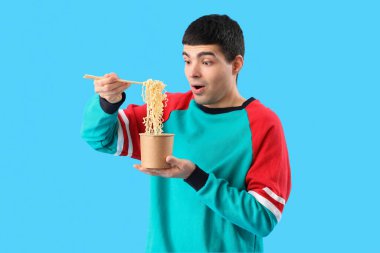 Mavi arka planda bir kase Çin eriştesi olan şaşırmış genç adam.