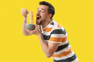 Handsome man with bowl of Chinese noodles on yellow background