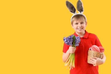 Tavşan kulaklı küçük çocuk, bir sepet kağıt yumurta ve sarı arka planda çiçekler.