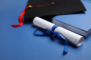 Mavi arka planda kurdeleli diploma ve mezuniyet şapkası.