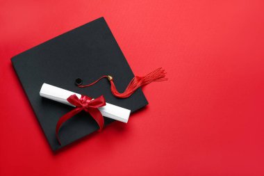 Kırmızı arka planda kurdeleli diploma ve mezuniyet şapkası.